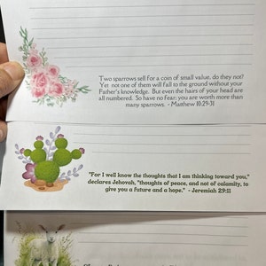 May include: A page from a journal with inspirational quotes from the Bible. The page features a watercolour illustration of pink flowers, a cactus, and a white lamb. The quotes are "Two sparrows sell for a coin of small value, do they not? Yet not one of them will fall to the ground without your Father's knowledge. But even the hairs of your head are all numbered. So have no fear; you are worth more than many sparrows. - Matthew 10:29-31" and "For I well know the thoughts that I am thinking toward you," declares Jehovah, "thoughts of peace, and not of calamity, to give you a future and a hope." - Jeremiah 29:11 and "Simon Peter answered: "You are the Christ, the Son of the living God." - Matthew 16:16
