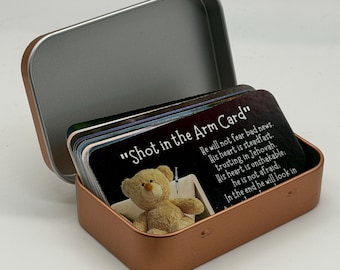 May include: A copper-colored metal tin containing a stack of rectangular cards. The front card features a tan teddy bear, a small syringe, and the text "Shot in the Arm Card" followed by religious scripture about trusting in Jehovah.