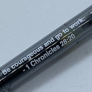 May include: A black pen with white text that reads "Be courageous and go to work. - 1 Chronicles 28:20"