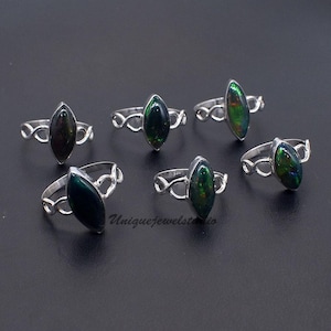 May include: Six silver rings with marquise-cut, dark green opal stones. The rings have a decorative infinity symbol design on the band. The opals have flashes of green and blue. The rings are displayed on a dark surface.