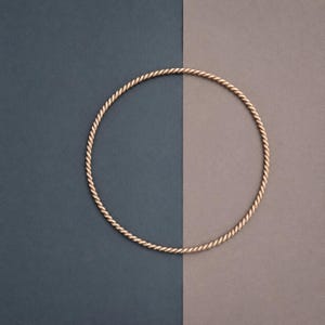 May include: A circular bangle bracelet crafted from a single continuous piece of rose gold metal. The surface of the bangle features a consistent twisted rope texture that runs along the entire circumference of the circular jewelry piece.