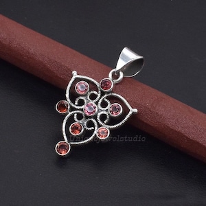 May include: A silver pendant with a delicate, intricate design featuring a cluster of pink gemstones. The pendant has a loop at the top for attaching to a chain.