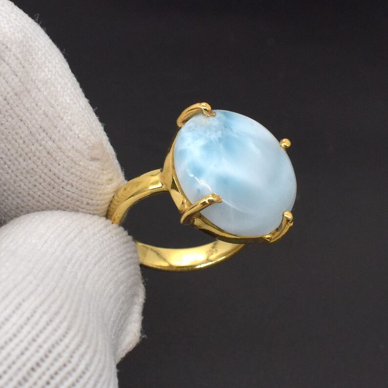 May include: A gold ring with a large oval-shaped blue and white gemstone. The gemstone has a cloudy, marbled appearance.