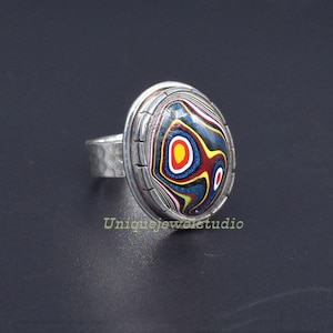 May include: A silver ring featuring a colourful agate stone set in a bezel. The stone displays a swirling pattern of red, yellow, blue and white.