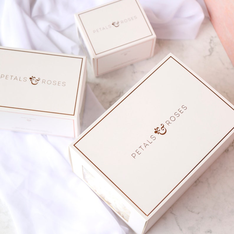 May include: Three white gift boxes with gold trim and the text "Petals & Roses" printed on the top of each box.