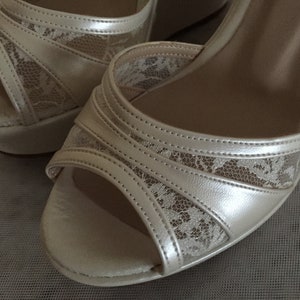 Pu&ograve; includere: Un paio di scarpe da sposa in raso avorio con delicati dettagli in pizzo. Le scarpe hanno un tacco a zeppa e una punta aperta.