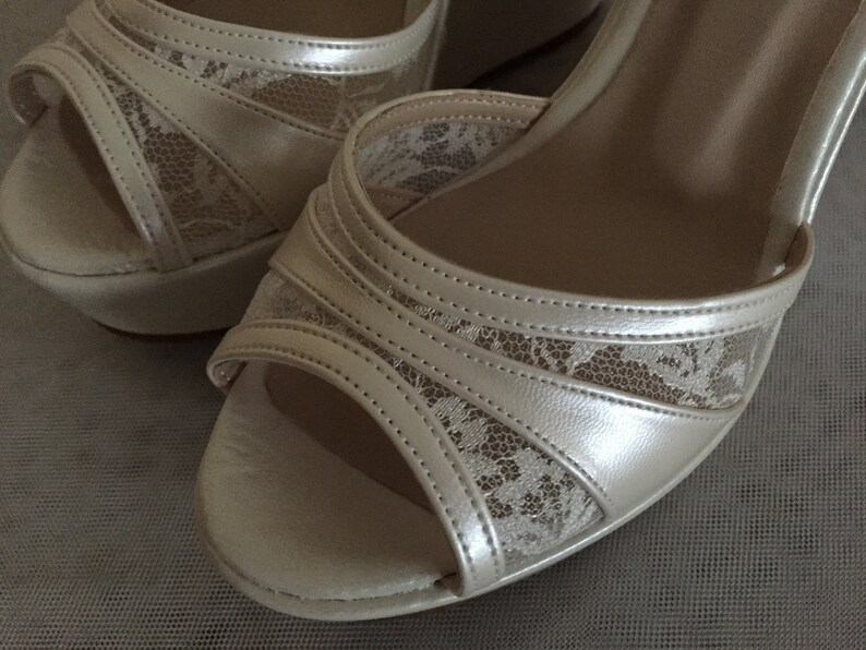 Pu&ograve; includere: Un paio di scarpe da sposa in raso avorio con delicati dettagli in pizzo. Le scarpe hanno un tacco a zeppa e una punta aperta.