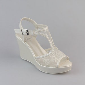 Può includere: Sandali con zeppa in pizzo bianco con chiusura a fibbia. I sandali hanno una suola platform e un design a T.
