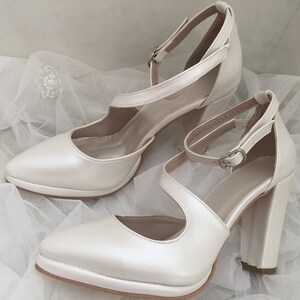 Pu&ograve; includere: Un paio di scarpe con tacco in raso bianco avorio con cinturini alla caviglia e punta a punta.