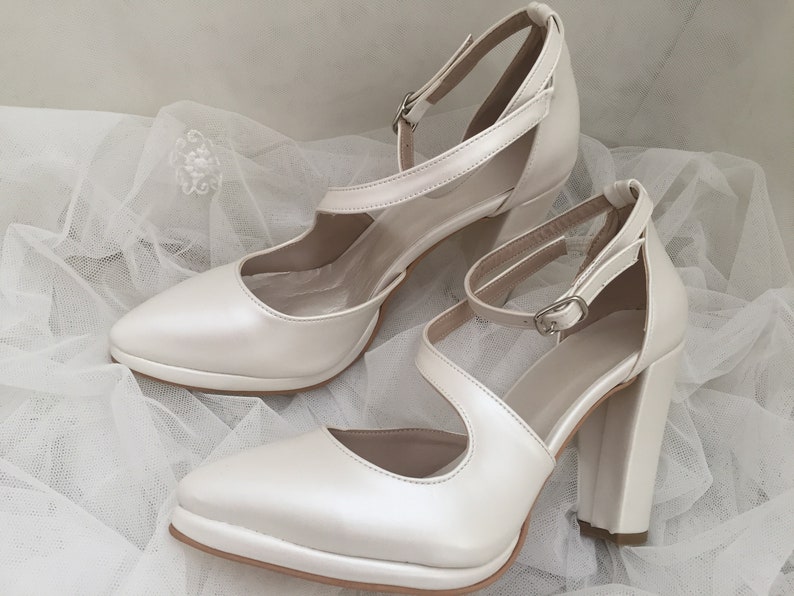 Pu&ograve; includere: Un paio di scarpe con tacco in raso bianco avorio con cinturini alla caviglia e punta a punta.