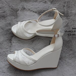Pu&ograve; includere: Sandali a zeppa color avorio con sovrapposizione in pizzo, tacco da 10 cm (3,9 pollici) e plateau da 2,5 cm.