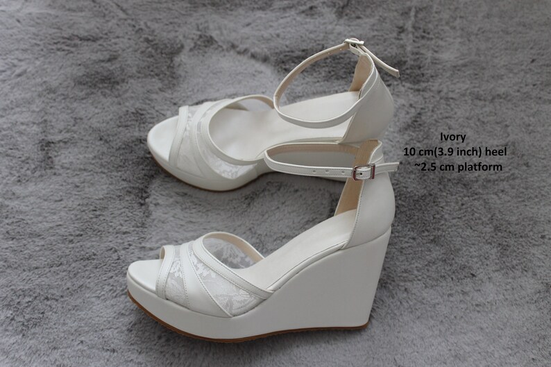 Pu&ograve; includere: Sandali a zeppa color avorio con sovrapposizione in pizzo, tacco da 10 cm (3,9 pollici) e plateau da 2,5 cm.
