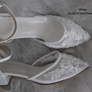 May include: White bridal shoes with a 4 cm (1.6 inch) heel height. The shoes are made of satin and have a delicate lace design with sequins.