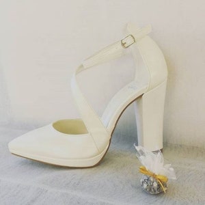 Pu&ograve; includere: Scarpe da sposa in raso bianco con punta a punta e tacco a blocco spesso. Le scarpe hanno un cinturino alla caviglia con chiusura a fibbia.