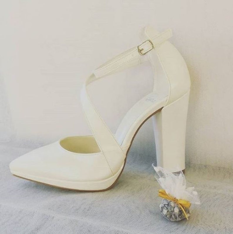 Pu&ograve; includere: Scarpe da sposa in raso bianco con punta a punta e tacco a blocco spesso. Le scarpe hanno un cinturino alla caviglia con chiusura a fibbia.