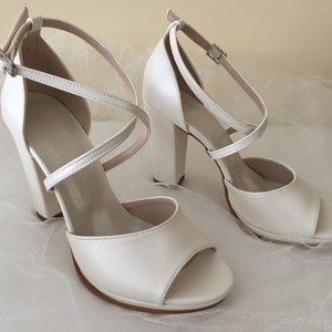 May include: A pair of white satin heeled sandals with a criss-cross strap design and an open toe.