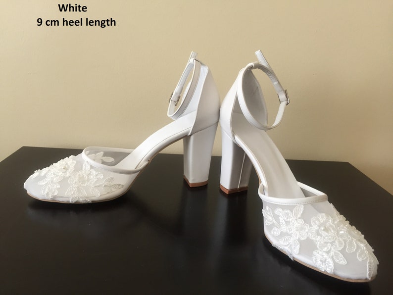 Pode incluir: Saltos brancos de noiva com um salto de 9 cm de altura. Os sapatos t&ecirc;m um delicado design de renda na ponta e na tira do tornozelo.