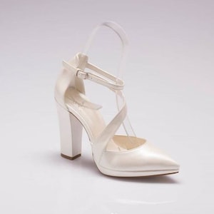 Pu&ograve; includere: Scarpe da sposa in raso bianco con punta a punta e tacco a blocco spesso. Le scarpe hanno un design a cinturino incrociato e una chiusura a fibbia.