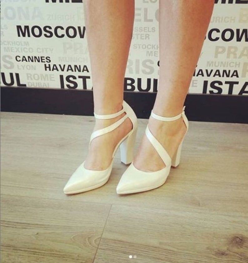 Pu&ograve; includere: Un paio di scarpe bianche con tacco alto, punta a punta e cinturini incrociati. Le scarpe hanno un tacco a blocco spesso.