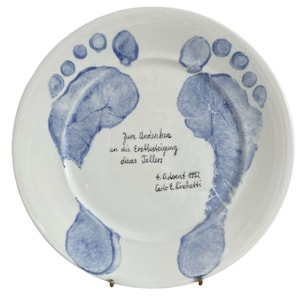 Peut inclure: Une assiette en céramique blanche avec deux empreintes de mains bleues et un message manuscrit qui dit "Zum Andenken an die Erbsheigung dieses Totels 4. Oktober 1993 Carlo &  Linochutti".