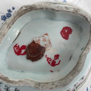 May include: Antique porcelain dish with a light blue interior and a textured, irregular rim. The dish features red markings and a brown wax seal. The bottom of the dish has a light blue color with some text.