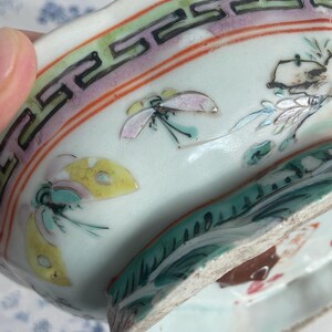 May include: Antique porcelain dish with a light blue interior and a decorative border featuring a repeating geometric pattern in black, green, and pink. The dish is adorned with hand-painted butterflies and floral motifs.