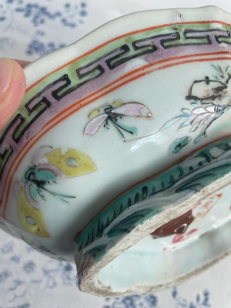 May include: Antique porcelain dish with a light blue interior and a decorative border featuring a repeating geometric pattern in black, green, and pink. The dish is adorned with hand-painted butterflies and floral motifs.
