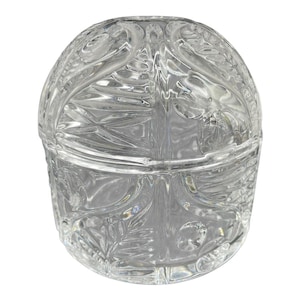 Op de afbeelding: Een heldere glazen pot met deksel, met een ovale vorm en gedetailleerde blad- en wervelpatronen. Het transparante glas laat licht door. De pot lijkt leeg en is waarschijnlijk voor decoratieve doeleinden.