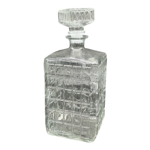 Puede incluir: Una decantador de vidrio transparente con cuerpo cuadrado y un patrón texturizado en forma de cuadrícula. La decantador tiene un tapón de vidrio transparente.