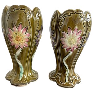 May include: Pair of green ceramic vases with floral designs. The vases have a scalloped rim and a flared base. The flowers are in shades of pink, yellow, and white.