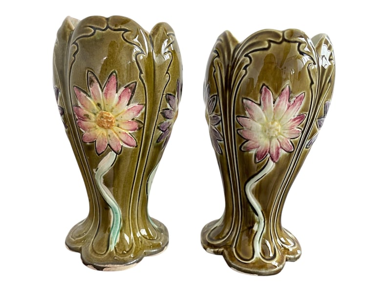 May include: Pair of green ceramic vases with floral designs. The vases have a scalloped rim and a flared base. The flowers are in shades of pink, yellow, and white.