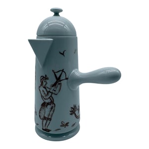 Puede incluir: Una cafetera de cerámica azul claro con cuerpo cilíndrico, tapa en forma de cúpula con un pequeño pomo, pico triangular y asa lateral. El exterior presenta dibujos de líneas de color marrón oscuro de una persona sosteniendo una ballesta y pequeñas plantas.