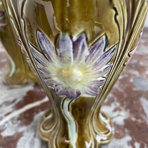 May include: A pair of ceramic table lamps with a green glaze and floral designs. The lamps feature a large flower with purple petals and a yellow center.