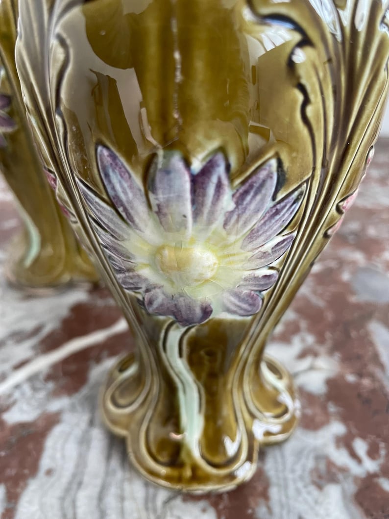 May include: A pair of ceramic table lamps with a green glaze and floral designs. The lamps feature a large flower with purple petals and a yellow center.
