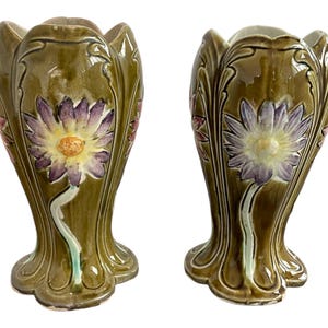 May include: A pair of green ceramic vases with floral designs. The vases have a scalloped rim and a wide base. The flowers are in shades of purple, pink, and yellow.