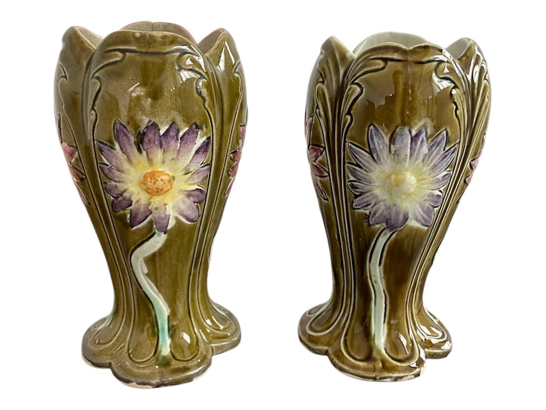 May include: A pair of green ceramic vases with floral designs. The vases have a scalloped rim and a wide base. The flowers are in shades of purple, pink, and yellow.