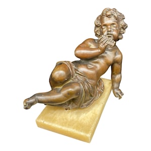 Peut inclure: Une sculpture en bronze d'un chérubin jouant de la flûte, reposant sur une base rectangulaire en albâtre.