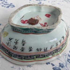 May include: An antique porcelain bowl with a light blue interior and exterior. The bowl features Chinese characters and decorative patterns in red, green, and black. The rim has a scalloped edge.