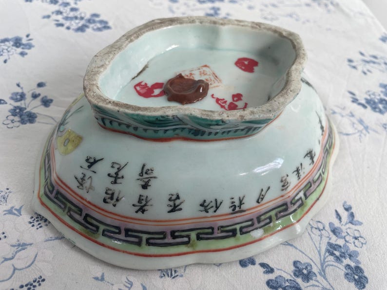 May include: An antique porcelain bowl with a light blue interior and exterior. The bowl features Chinese characters and decorative patterns in red, green, and black. The rim has a scalloped edge.