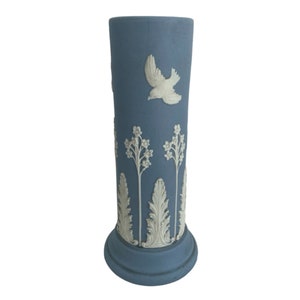 Può includere: Un vaso in ceramica blu con disegni floreali e di uccelli bianchi. Il vaso ha una forma cilindrica con una base svasata.