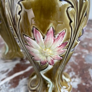 May include: A pair of green ceramic vases with floral designs. The vases have a raised, textured design with a flower in the center. The flowers are pink, white, and green.
