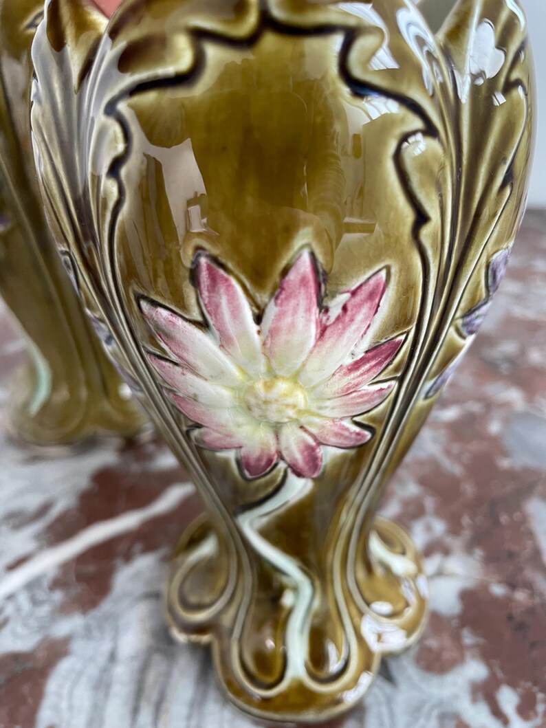 May include: A pair of green ceramic vases with floral designs. The vases have a raised, textured design with a flower in the center. The flowers are pink, white, and green.