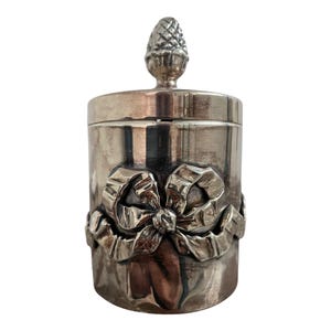 May include: Silver jar with a decorative bow and a pinecone-shaped lid.