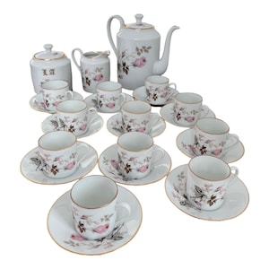 Op de afbeelding: Een wit porseleinen theeservies met een roze rozenpatroon. De set bevat een theepot, een roomkan, een suikerpot en 10 kopjes en schoteltjes.