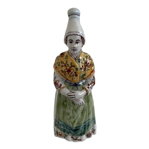 May include: A ceramic figurine of a woman wearing a white cap, a yellow and green shawl, and a green dress with floral details.