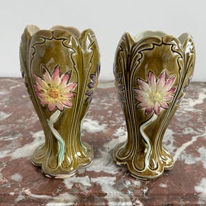 May include: A pair of green ceramic vases with floral designs. The vases have a scalloped rim and a flared base. The flowers are painted in shades of pink, white, and yellow.