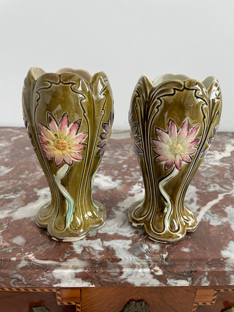 May include: A pair of green ceramic vases with floral designs. The vases have a scalloped rim and a flared base. The flowers are painted in shades of pink, white, and yellow.