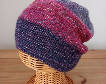 May include: A knitted hat with a pink, blue, and gray striped pattern. The hat is displayed on a wicker hat stand.