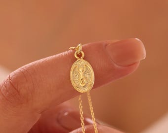 May include: Gold necklace with a pendant featuring a stylized human figure with a spiral design. The pendant is oval shaped and has a textured surface.