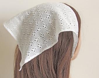 May include: White cotton eyelet lace headscarf with a delicate floral pattern. The scarf is tied around the head and falls down the back.